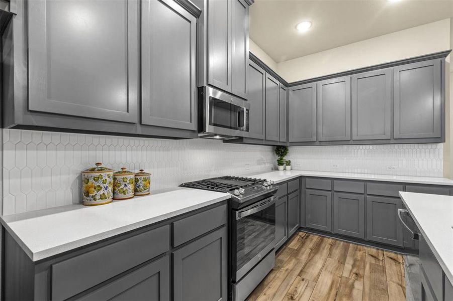 Kitchen featuring stainless steel appliances, light countertops, light wood finished floors, and gray cabinetry