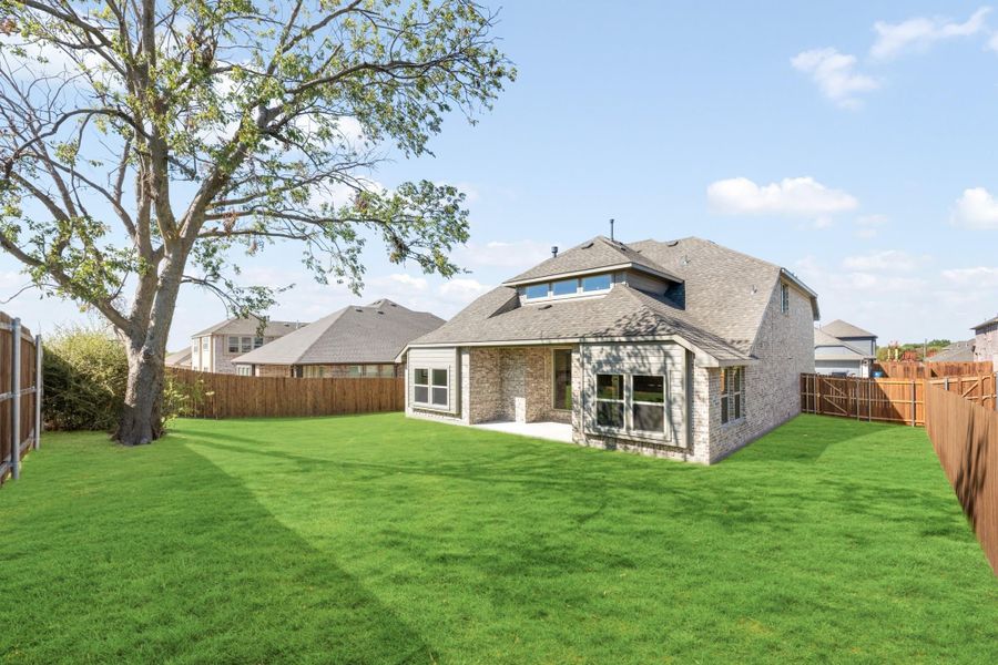 Brick home rear exterior with large fenced backyard, green lawn, and mature tree Brick home rear exterior with large fenced backyard, green lawn, and mature tree