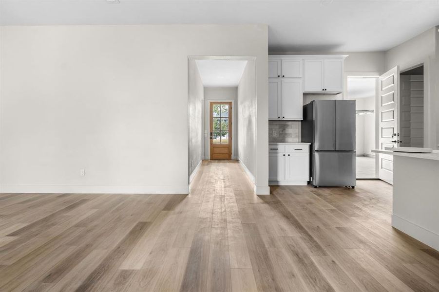 Kitchen featuring white cabinets, freestanding refrigerator, light wood-type flooring, backsplash, and light countertops