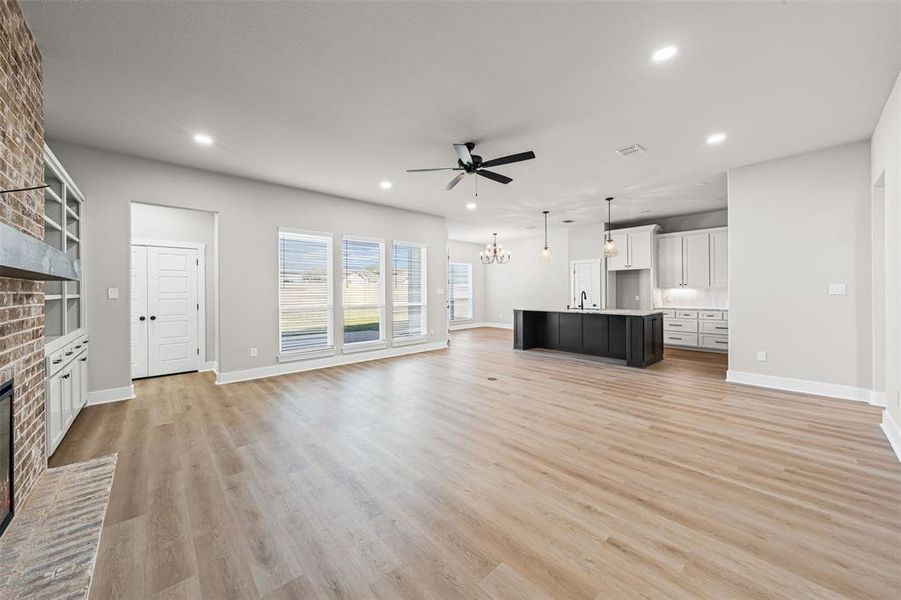 Unfurnished living room featuring a fireplace, light wood-type flooring, a chandelier, ceiling fan, and recessed lighting Unfurnished living room featuring a fireplace, light wood-type flooring, a chandelier, ceiling fan, and recessed lighting