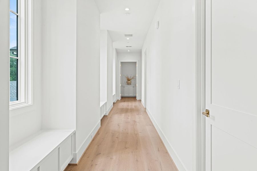 A thoughtfully designed upstairs hallway leads to the primary suite, creating a beautiful sense of arrival. Three large windows w/ built-in window seats & storage below bring in natural light, while secondary bedrooms are positioned on the opposite side. French doors open to the primary suite, offering a glimpse into the elegant entry beyond. A thoughtfully designed upstairs hallway leads to the primary suite, creating a beautiful sense of arrival. Three large windows w/ built-in window seats & storage below bring in natural light, while secondary bedrooms are positioned on the opposite side. French doors open to the primary suite, offering a glimpse into the elegant entry beyond.