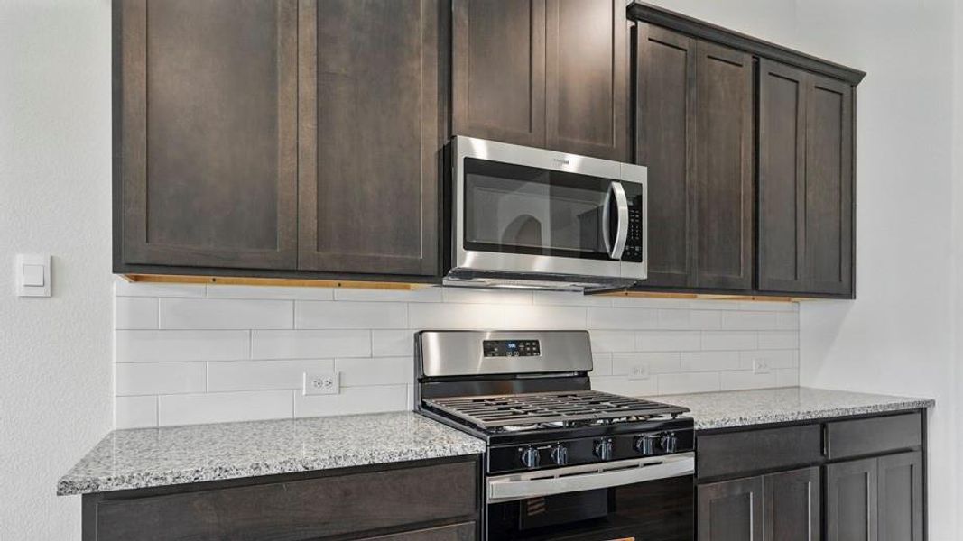 Kitchen featuring dark wood cabinetry, light speckled countertops, a stainless steel range with an overhead microwave, and a white subway tile backsplash