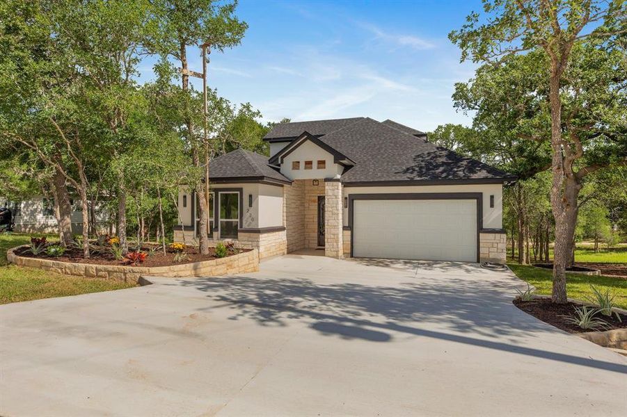 View of front of property featuring stone siding, stucco siding, driveway, and a garage