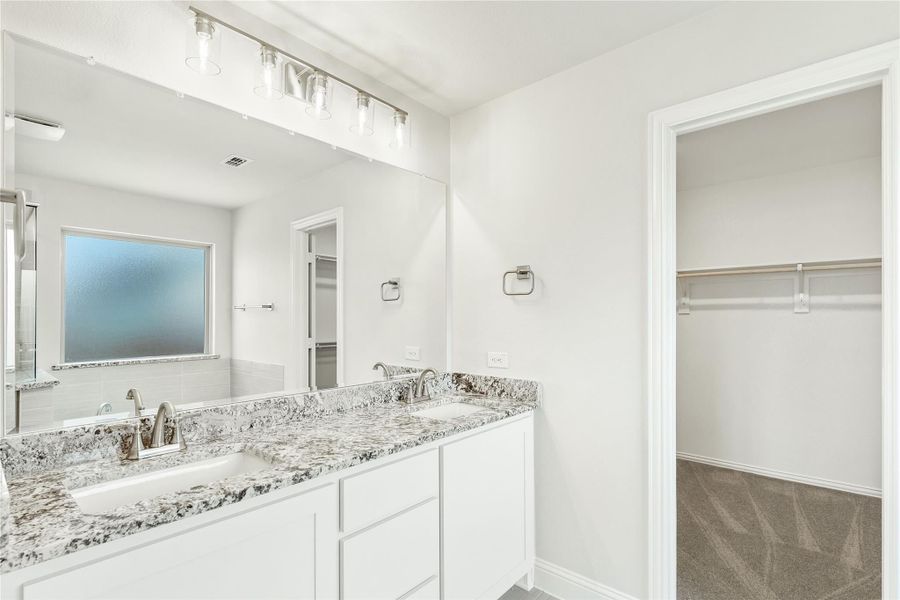 Bathroom with double sink vanity, granite countertops, large mirror, and walk-in closet entrance
