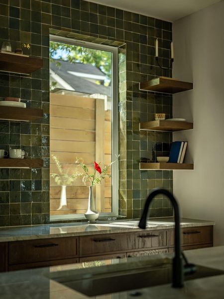 Rich tilework and open shelving surround a large window over the polished stone countertop. Rich tilework and open shelving surround a large window over the polished stone countertop.