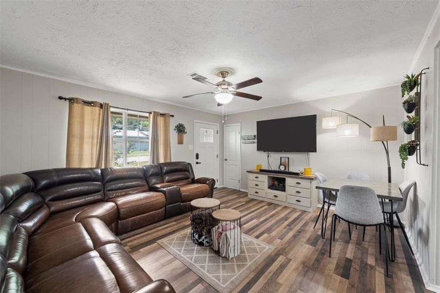 Living area with wood finished floors, a textured ceiling, a ceiling fan, a decorative wall, and ornamental molding Living area with wood finished floors, a textured ceiling, a ceiling fan, a decorative wall, and ornamental molding