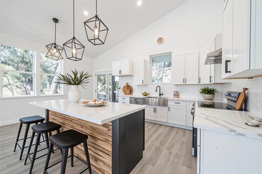 Kitchen with a kitchen island, stainless steel appliances, light wood finished floors, pendant lighting, and light stone countertops