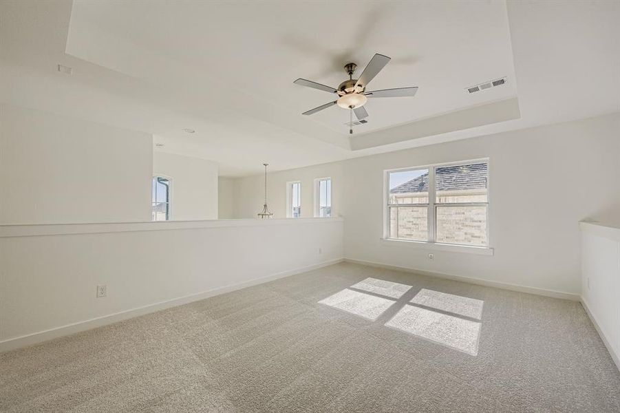 Unfurnished room with a raised ceiling, light carpet, ceiling fan, and a chandelier