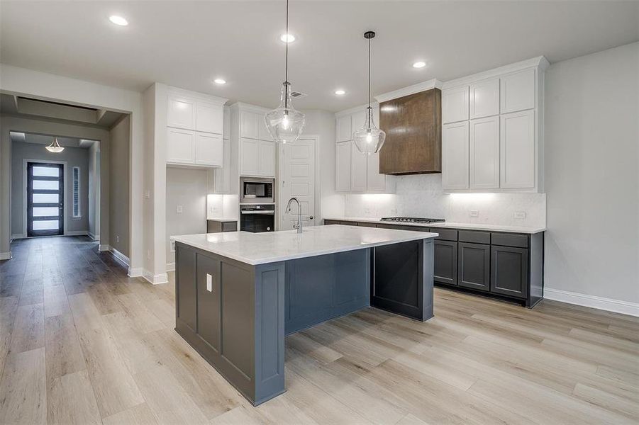 Kitchen featuring light hardwood / wood-style flooring, decorative light fixtures, a kitchen island with sink, white cabinets, and appliances with stainless steel finishes