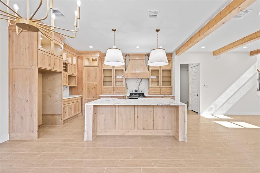 Kitchen featuring light wood finish cabinetry, glass fronted cabinets, light stone counters, a large island with sink, and beam ceiling Kitchen featuring light wood finish cabinetry, glass fronted cabinets, light stone counters, a large island with sink, and beam ceiling