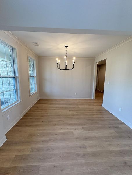 Spacious interior room featuring wood-finish flooring, two large windows, a modern chandelier, neutral wall tones, and white trim
