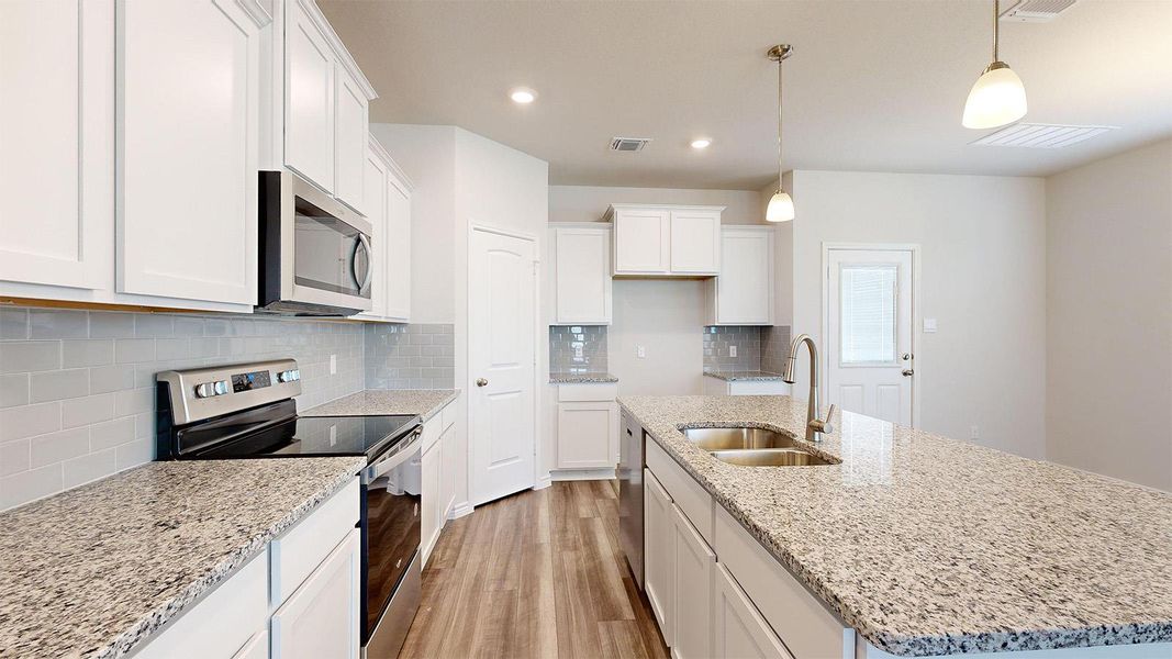 Kitchen featuring stainless steel appliances, decorative backsplash, light wood-style floors, and light stone countertops