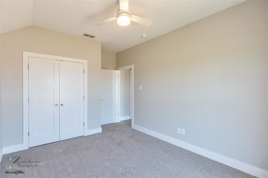 Unfurnished bedroom featuring carpet, a closet, a ceiling fan, and vaulted ceiling