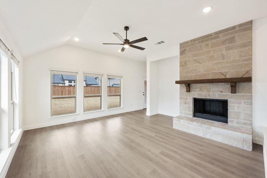 Open living room with vaulted ceiling, ceiling fan, stone fireplace, and hardwood floors Open living room with vaulted ceiling, ceiling fan, stone fireplace, and hardwood floors