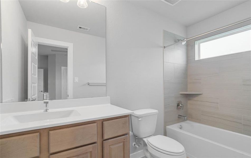 Secondary bath features tile flooring, bath/shower combo with tile surround, white stained wood cabinets, beautiful light countertops, mirror, dark, sleek fixtures and modern finishes.