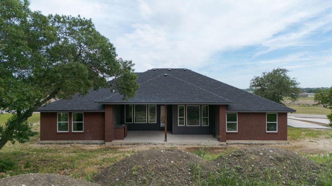 Rear view of property featuring roof with shingles, brick siding, and a patio area