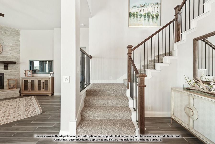 Carpeted staircase with wood and iron railing, tile floor entryway, and stone fireplace visible in adjacent living room. Carpeted staircase with wood and iron railing, tile floor entryway, and stone fireplace visible in adjacent living room.