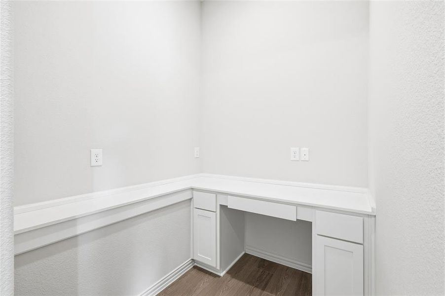 Unfurnished office with built in study area, dark wood-type flooring, and a textured wall