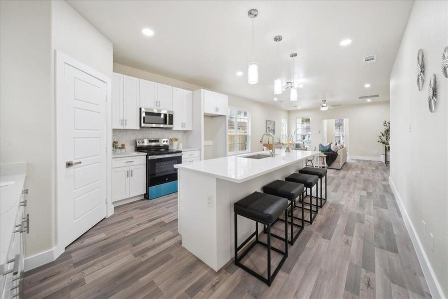 Kitchen with stainless steel appliances, decorative light fixtures, a kitchen island with sink, a breakfast bar, and white cabinets