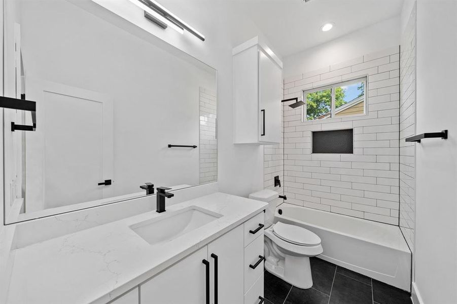 Full bathroom featuring vanity, tiled shower / bath combo, toilet, and tile patterned flooring