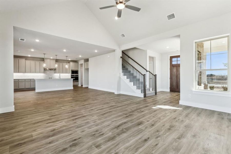 Unfurnished living room with hardwood / wood-style floors, high vaulted ceiling, and ceiling fan
