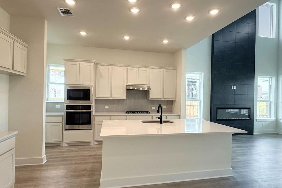 A contemporary kitchen and living area featuring a spacious island and a striking floor-to-ceiling fireplace. A contemporary kitchen and living area featuring a spacious island and a striking floor-to-ceiling fireplace.