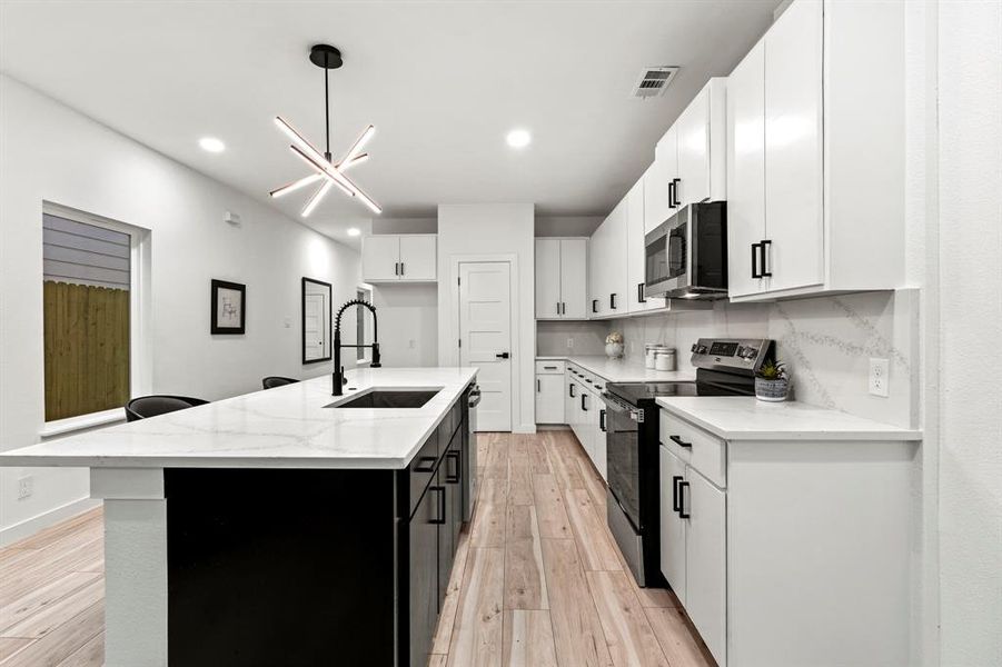 Kitchen featuring appliances with stainless steel finishes, a sink, light wood-style flooring, a kitchen island with sink, and white cabinets Kitchen featuring appliances with stainless steel finishes, a sink, light wood-style flooring, a kitchen island with sink, and white cabinets