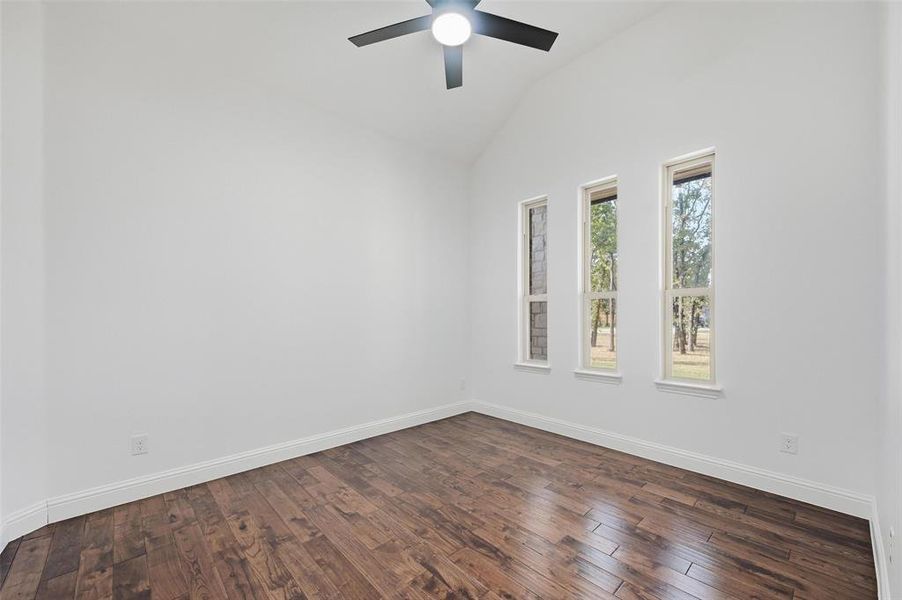 Empty room with lofted ceiling, dark wood-style flooring, and a ceiling fan