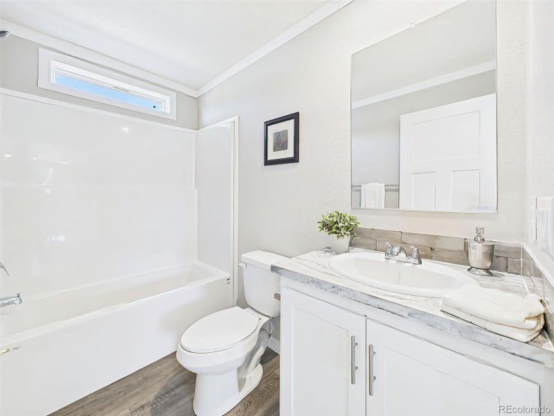 Hall Bathroom – A full bath with a tub-shower combo, sleek tile backsplash, and stylish marble-look counters over white cabinetry.