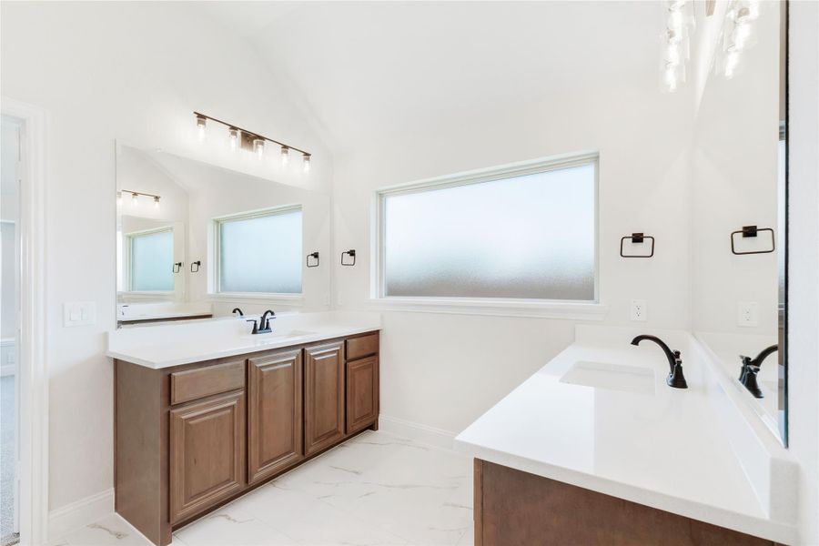 Bathroom with dual vanities, wood cabinets, white countertops, and marble tile floors Bathroom with dual vanities, wood cabinets, white countertops, and marble tile floors