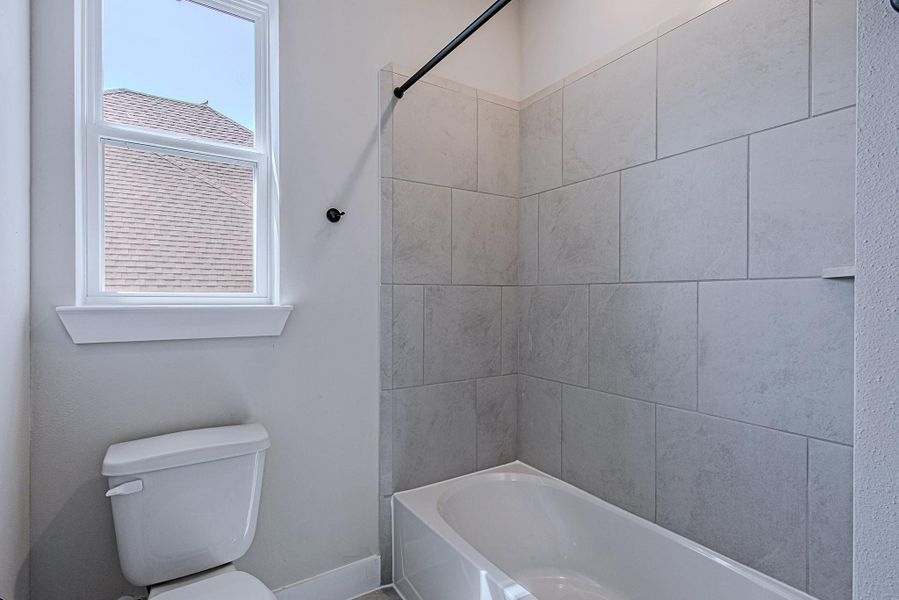 Bathroom with a tub-and-shower combination, tile surround, and natural light