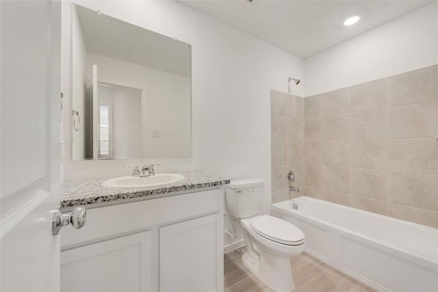 Full bathroom with vanity, tiled shower / bath, hardwood / wood-style flooring, and toilet