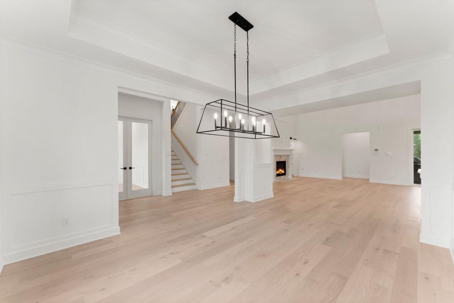 Dining area features light hardwood floors, a modern chandelier, and a cozy fireplace. It has an open layout with tray ceiling Dining area features light hardwood floors, a modern chandelier, and a cozy fireplace. It has an open layout with tray ceiling