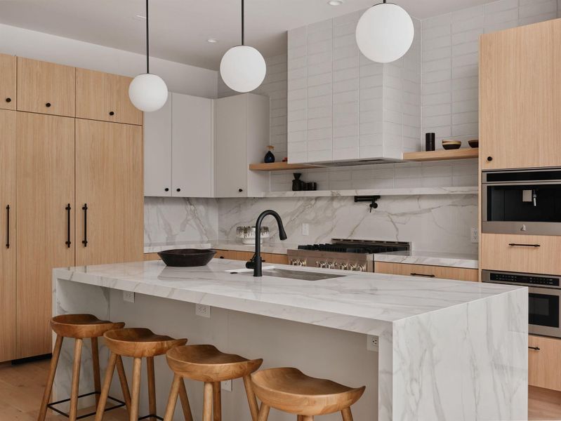 Kitchen featuring a waterfall island with a stone surface and undermount sink, complemented by wood-finish and white cabinetry