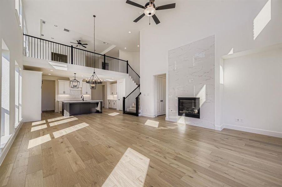 Unfurnished living room with a high ceiling, a high end fireplace, a ceiling fan, stairway, and light wood-style flooring
