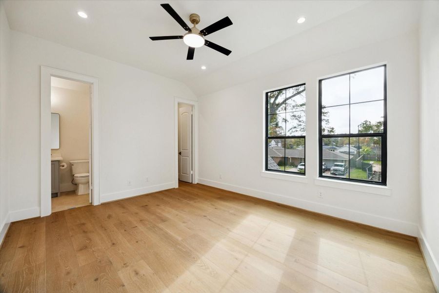 Fourth bedroom with white oak wood flooring, recessed lighting, ceiling fan, and ensuite half-bath access.