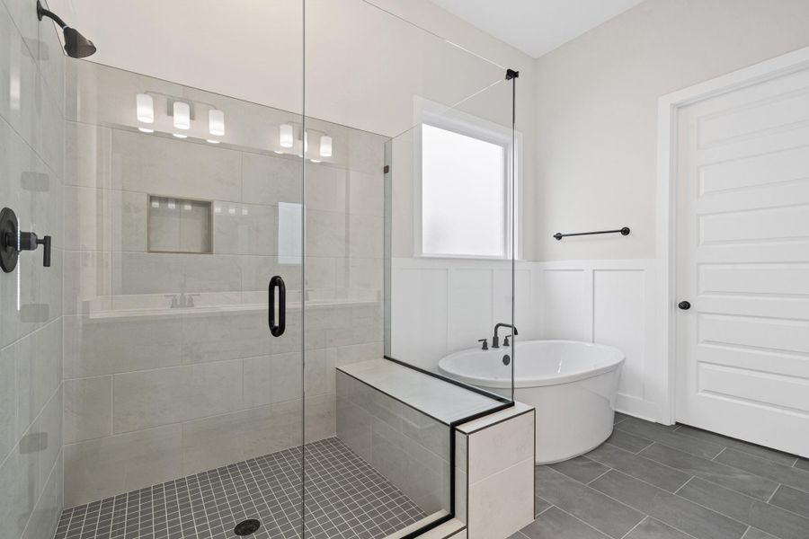 Glass-enclosed shower with matte black fixtures, built-in shower bench, recessed shower niche, freestanding soaking tub, and plank-style floor tiling Glass-enclosed shower with matte black fixtures, built-in shower bench, recessed shower niche, freestanding soaking tub, and plank-style floor tiling