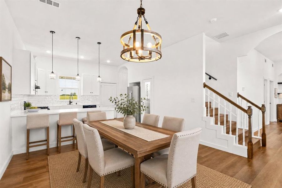 Open-concept living area featuring wood-finish flooring, a contemporary kitchen with white cabinetry and subway tile backsplash, and a staircase with white risers and wood handrails