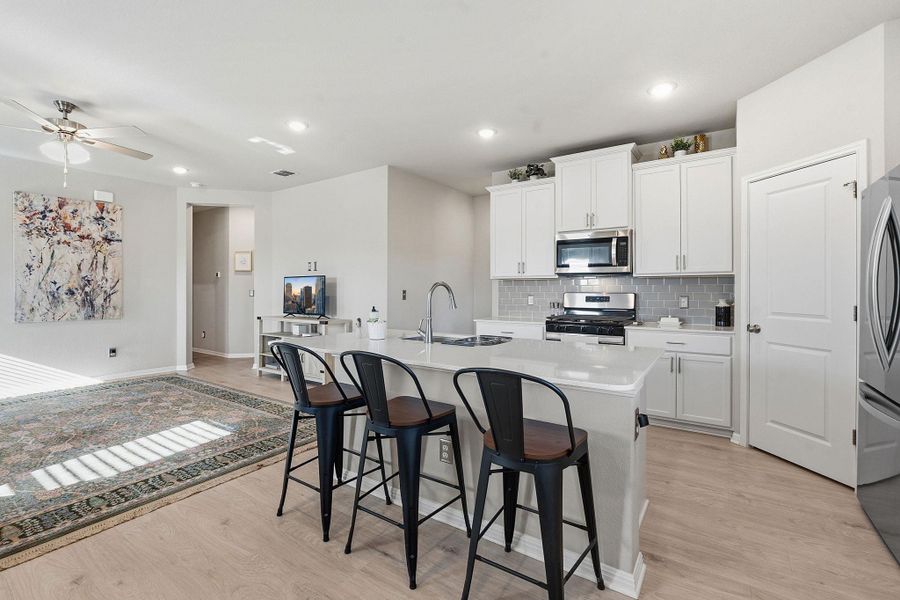 Kitchen featuring a kitchen breakfast bar, stainless steel appliances, white cabinetry, a ceiling fan, and light wood finished floors Kitchen featuring a kitchen breakfast bar, stainless steel appliances, white cabinetry, a ceiling fan, and light wood finished floors