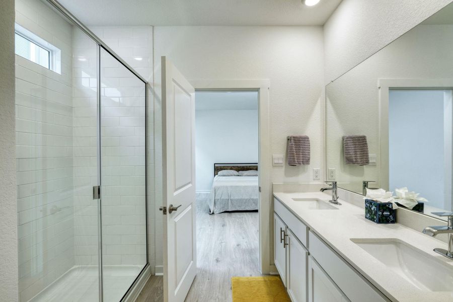 Ensuite bathroom with a stall shower, connected bathroom, a sink, and wood finished floors