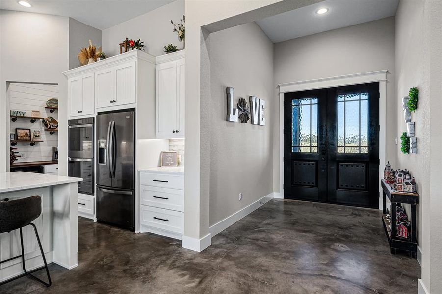 Kitchen featuring white cabinetry, finished concrete flooring, black fridge, recessed lighting, and double oven Kitchen featuring white cabinetry, finished concrete flooring, black fridge, recessed lighting, and double oven