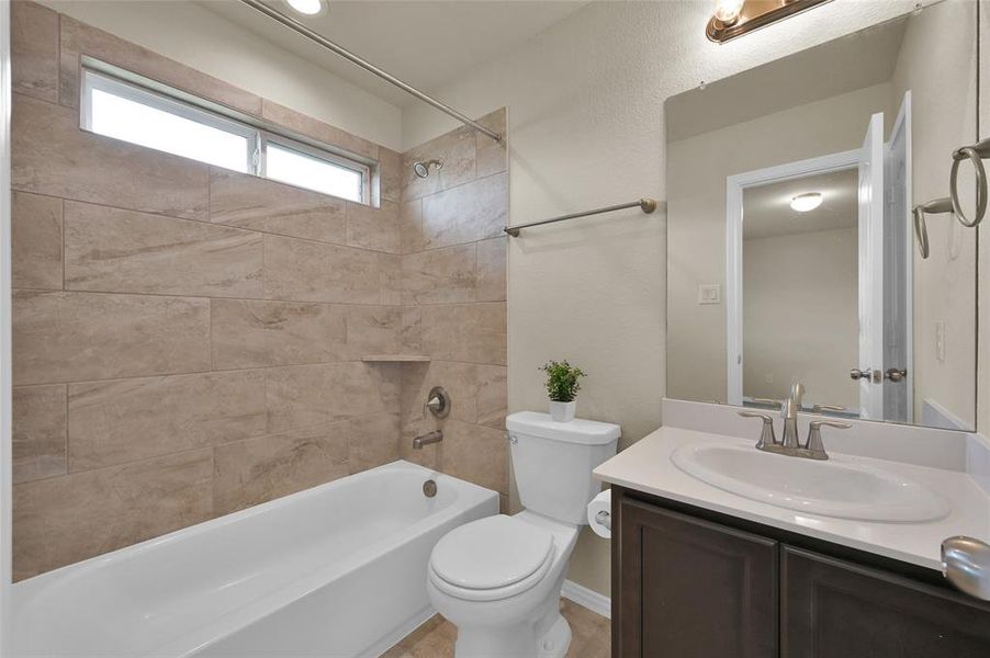 This is a modern bathroom featuring a large bathtub with beige tile surround, a single sink vanity with counter space, and natural light from a high window.