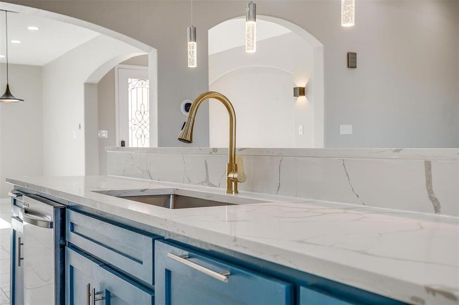 Kitchen featuring blue cabinetry, sink, hanging light fixtures, light stone counters, and stainless steel dishwasher