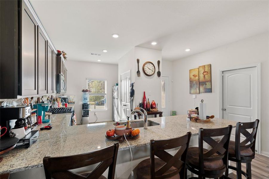 Kitchen with a peninsula, a breakfast bar area, light stone counters, dark wood finished floors, and recessed lighting