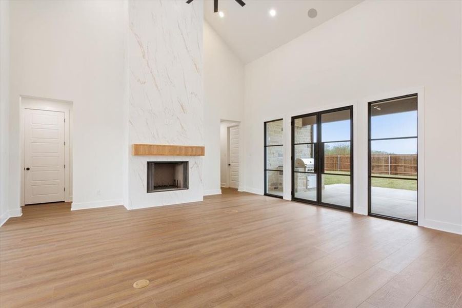 Unfurnished living room with high vaulted ceiling, light wood-type flooring, a premium fireplace, and a ceiling fan