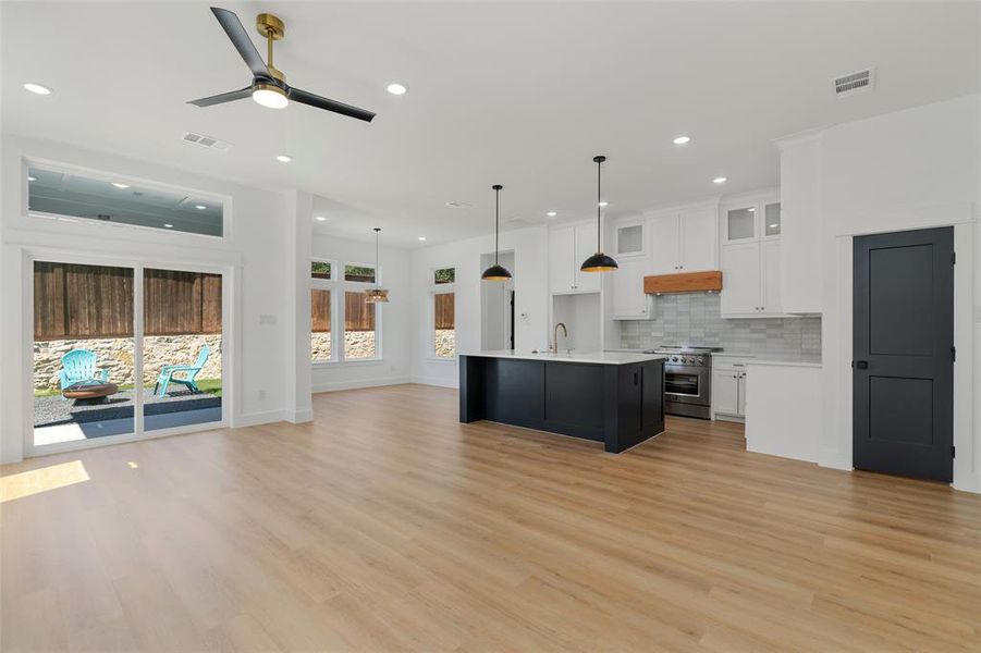 Kitchen featuring pendant lighting, a kitchen island with sink, white cabinets, high end range, and ceiling fan