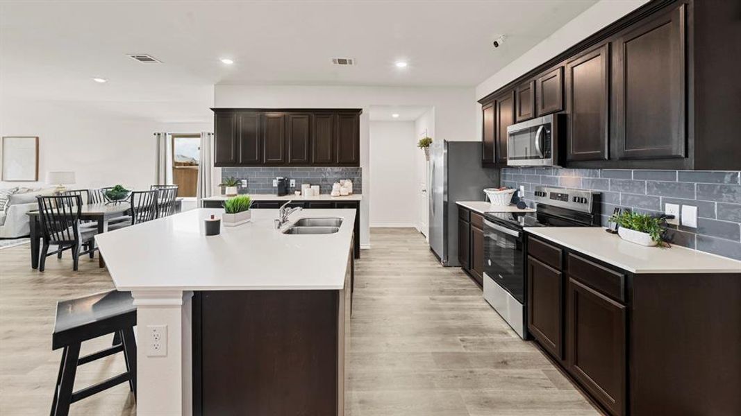 The kitchen features dark wood cabinetry, stainless steel appliances, light countertops, and a gray subway tile backsplash