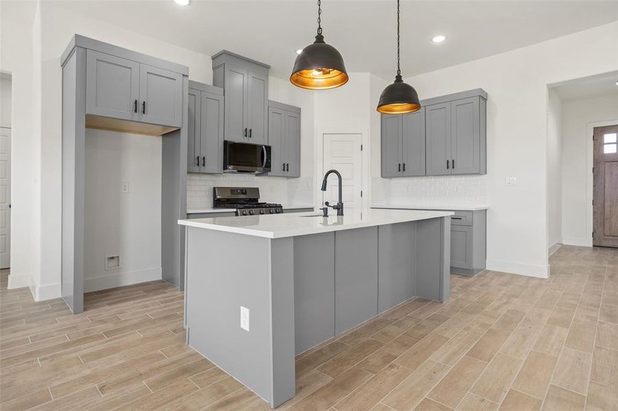 Kitchen with gray cabinetry, a kitchen island with sink, stainless steel appliances, and backsplash