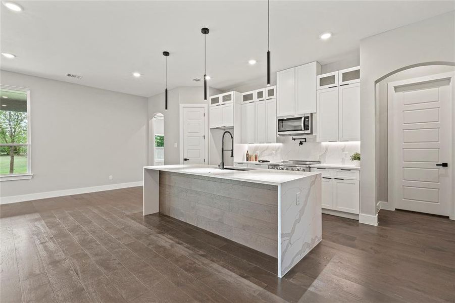 Kitchen featuring appliances with stainless steel finishes, arched walkways, dark wood finished floors, an island with sink, and recessed lighting