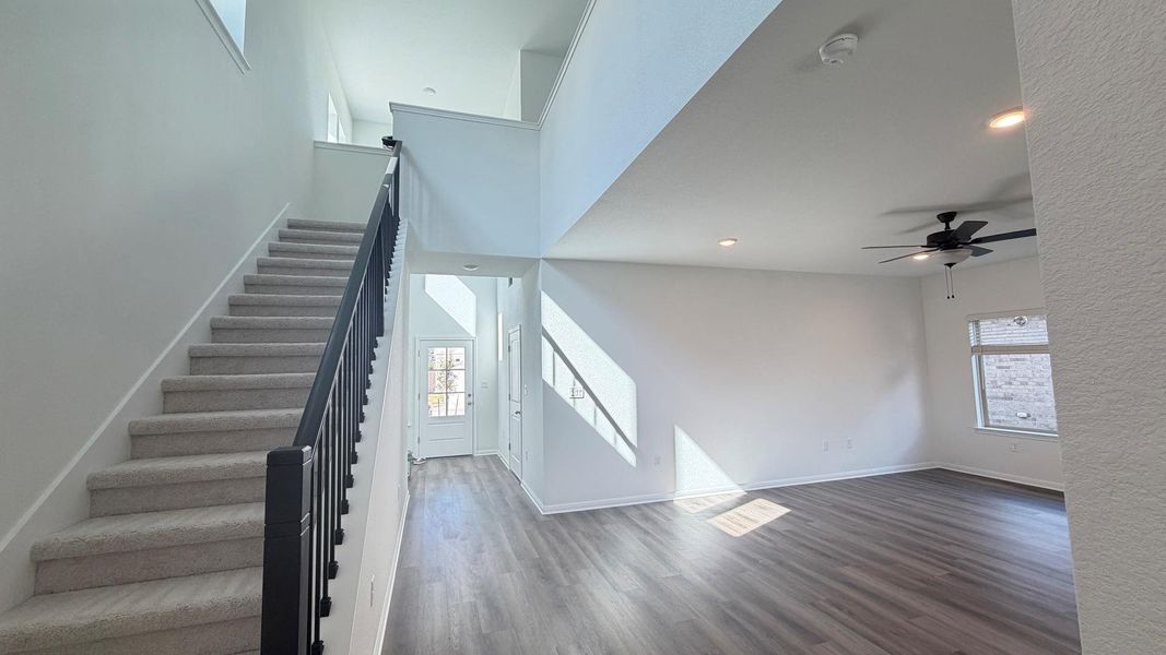 A spacious entry and living area features high ceilings, light wood-look flooring, and a carpeted staircase leading to the upper level. A spacious entry and living area features high ceilings, light wood-look flooring, and a carpeted staircase leading to the upper level.